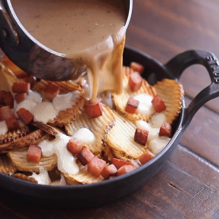 SPAM® poutine fries served in a cast iron skillet on a wooden table.